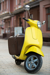 Brown suitcase on yellow scooter. Scooter on street background. Things are packed. Luggage for a small trip.