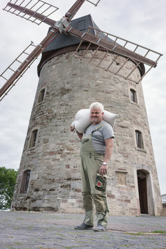 Senior miller with flour sack posing in front of medieval windmill