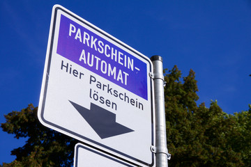 Schild Parkscheinautomat mit Text "Hier Parkschein lösen" in Aachen vor blauem Himmel und Bäumen