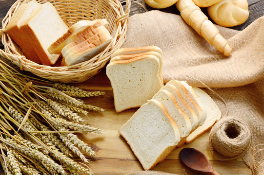 Many bread  in the basket on wooden floor with sack cloths. 
Kaiser roll and sliced white bread .
