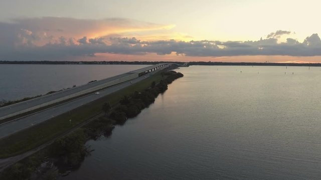 Aerial pan of car driving over Florida inter coastal bridge into the sunset.