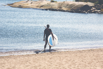 An unidentified man is carrying a surf board after the run in the ocean. Image has a vintage effect applied.