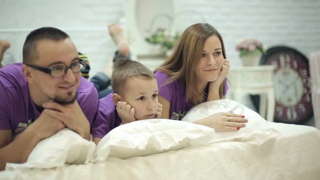 Happy family takes a photo lying on a bed .