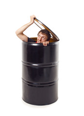 man looks out of a black barrel. the guy hid in a barrel. the young man lifted the lid and peeking out of the black barrel. isolated on white background