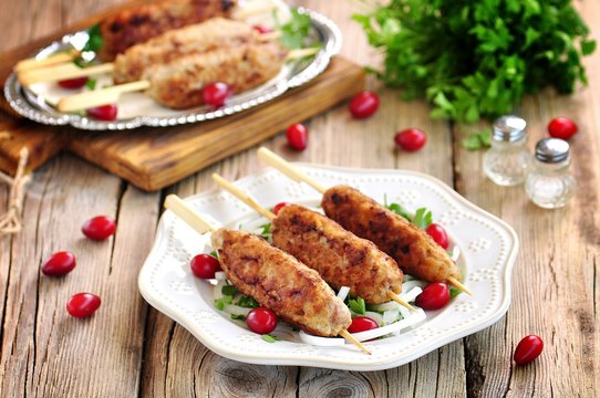 Homemade meat kebabs skewers with dogberry and onion salad on wooden background.
