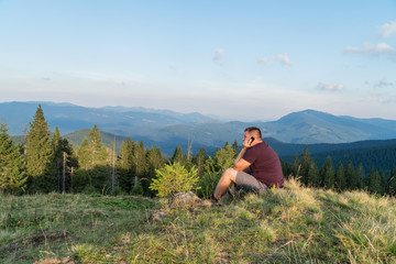 Naklejka na ściany i meble Man are sitting on a hill in mountains and talking on the phone