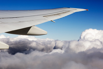 The wing of the plane on sky background. Aerial view of thick clouds over the land, the landscape.