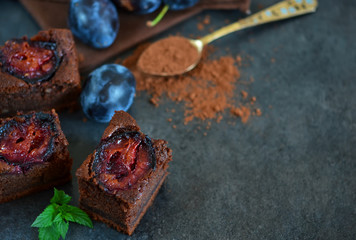 Chocolate cake with plums on a dark background with milk