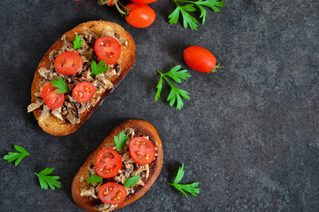 Toasts with sprats, tomato and garlic on a black background with