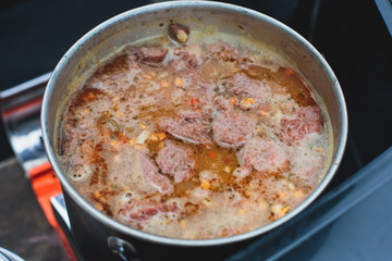 A concept of cooking field red colored meat soup on a bonfire or portable gas stove on camping in Norway