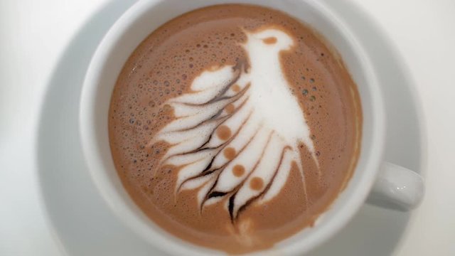 Slow motion close-up shot of stirring up the coffee with cream bird picture on the foam