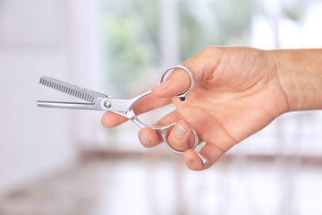 Hairdresser holding professional scissors on blurred background