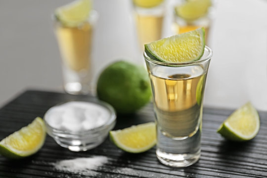 Shot of gold tequila with lime slices and salt on wooden board