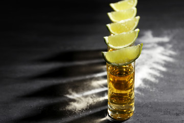 Gold tequila shots with lime and salt on gray background
