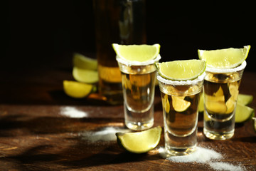 Gold tequila shots with lime and salt on wooden table