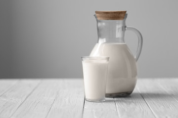 Jug and glass of fresh milk on white wooden table