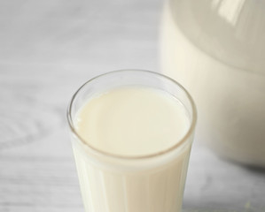 Glass of fresh milk and jug on light blurred background