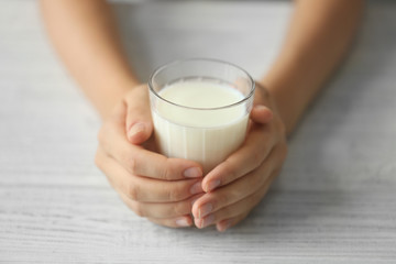 Female hands holding glass of fresh milk on light wooden background
