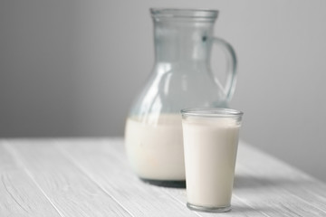 Jug and glass of fresh milk on white wooden table