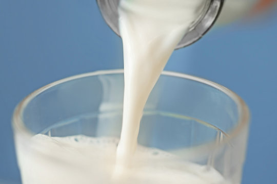 Milk pouring from a bottle into a glass on blue background, closeup