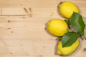 three lemons with leaves on wooden table
