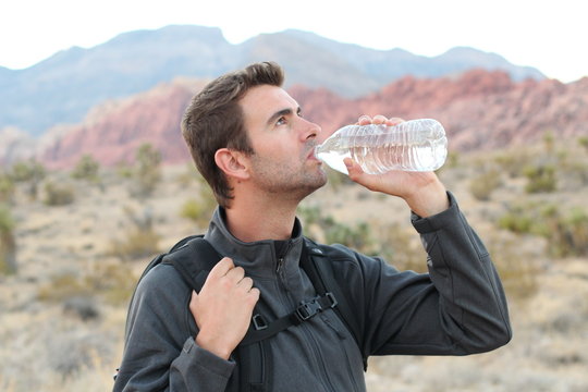 Side view of young man drinking water while standing during a hike