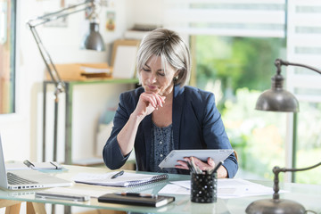 a middleage woman sitting at her desk working with a tablet