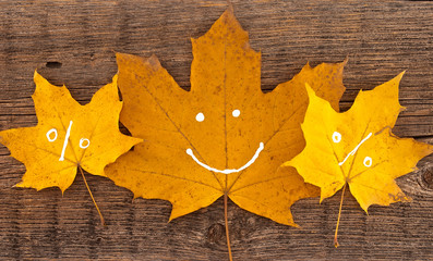 Naklejka na ściany i meble Autumn leaves with smile on rustic wooden background. 