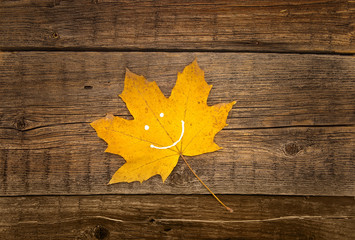 Naklejka na ściany i meble Autumn yellow leaf with smile on rustic wooden background. 