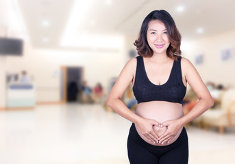 Fototapeta na wymiar Pregnant Woman holding her hands in a heart shape on her belly i