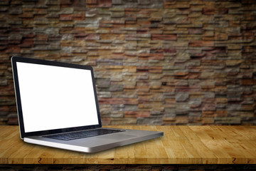 Empty screen Laptop on wood bench plans in front of a sand stone wall.background.