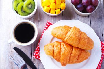 Top view of healthy breakfast with croissants, black coffee and fruits on a wooden table.