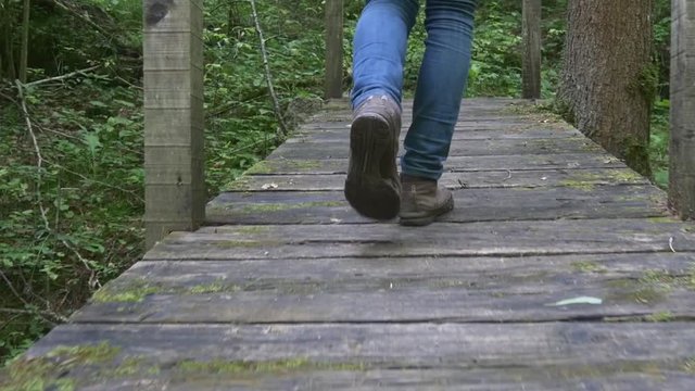 Legs of female hiker walk across a wooden bridge