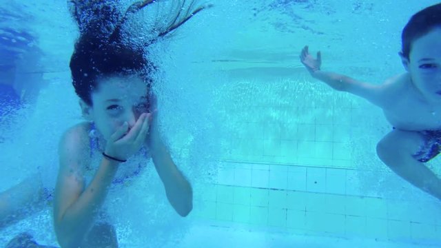 Underwater footage of two kids jumping into a swimming pool and diving in the water