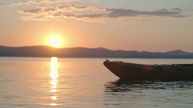 Lockdown of male tourist paddling kayak on lake in slow motion, sun setting behind chain of mountains in background 