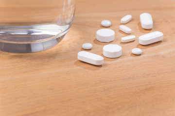 Fototapeta na wymiar White pills with glass of water on wood background