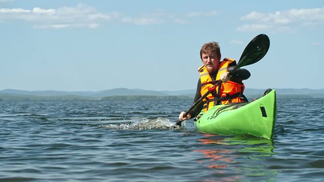 Slow motion lockdown of man with beard practicing paddling with forward sweep strokes on touring kayak on sunny summer day