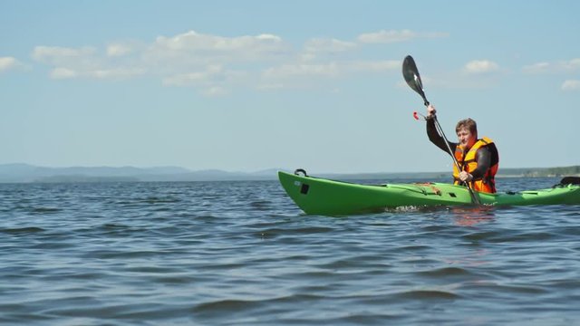 Tracking surface level shot of male tourist practicing paddling kayak along blue lake on beautiful summer day
