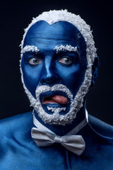 Man painted in blue color with snowy hair and beard grimacing on black background