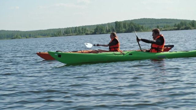 Slow motion tracking of tourist couple enjoying lake kayaking on sunny summer day