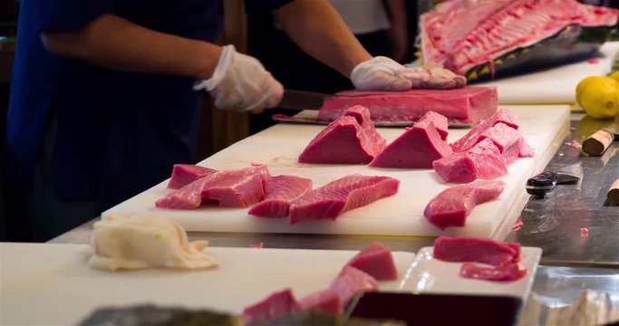 Chef hands cutting with knife raw bluefin tuna filet pieces 4k video in sushi restaurant kitchen. Asian japanese cuisine.