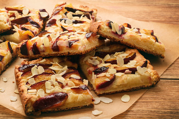 Slices of plum pie on brown wooden background.
