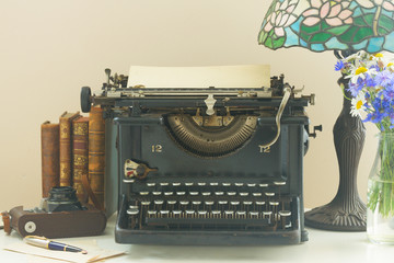 black vintage typewriter with books on wooden table with art nuveau lamp close up
