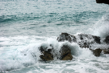 A small sea wave crashing on the rocks near the shore