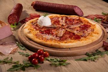 Pizza served on wooden board and raw ingredients on table