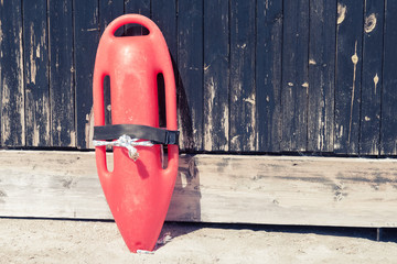 Close up of red lifeguard rescue can equipment against the wooden tower wall at the sandy beach.  - Powered by Adobe