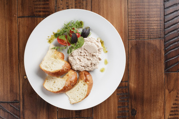 Rabbit pate with salad and bread in a white plate. White meat fillet. Wooden background.