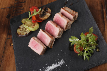 Tuna fillet slices with salad on a slate. Wooden background