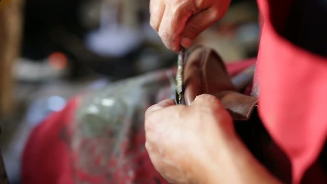 Calzolaio al Lavoro nella sua bottega artigianale. Attaccatura della suola ad un mocassino. 