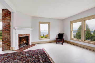 Empty traditional room interior in white tones with brick fireplace and rug